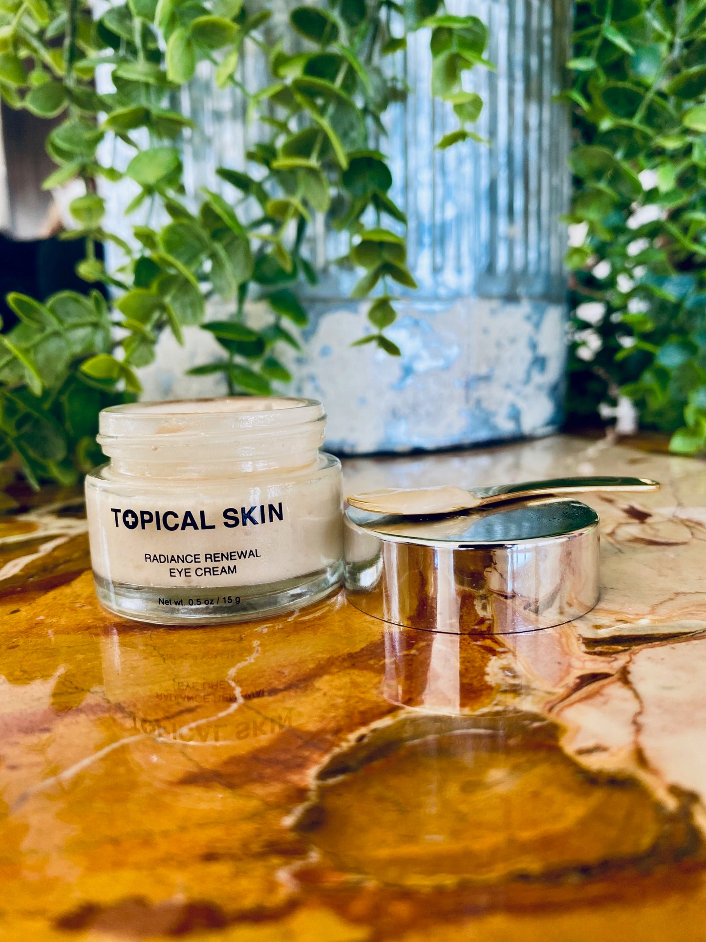 Topical Skin Radiance Renewaleye cream jar on a marble surface with plants in the background