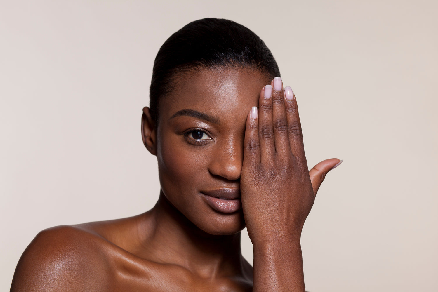 Woman with a hand covering one eye against a beige background