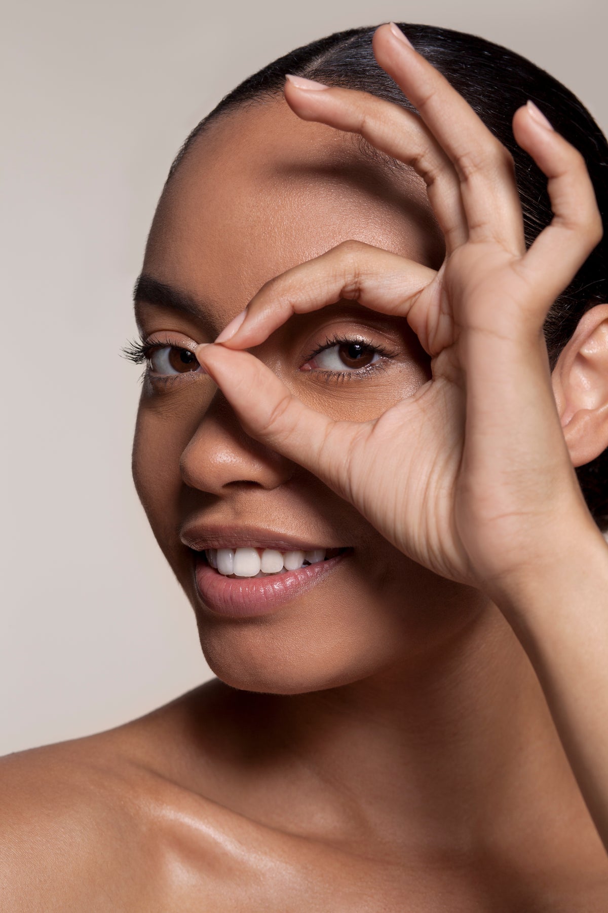 Close-up of a woman covering her eyes with her hands, showing smooth skin and short dark hair.