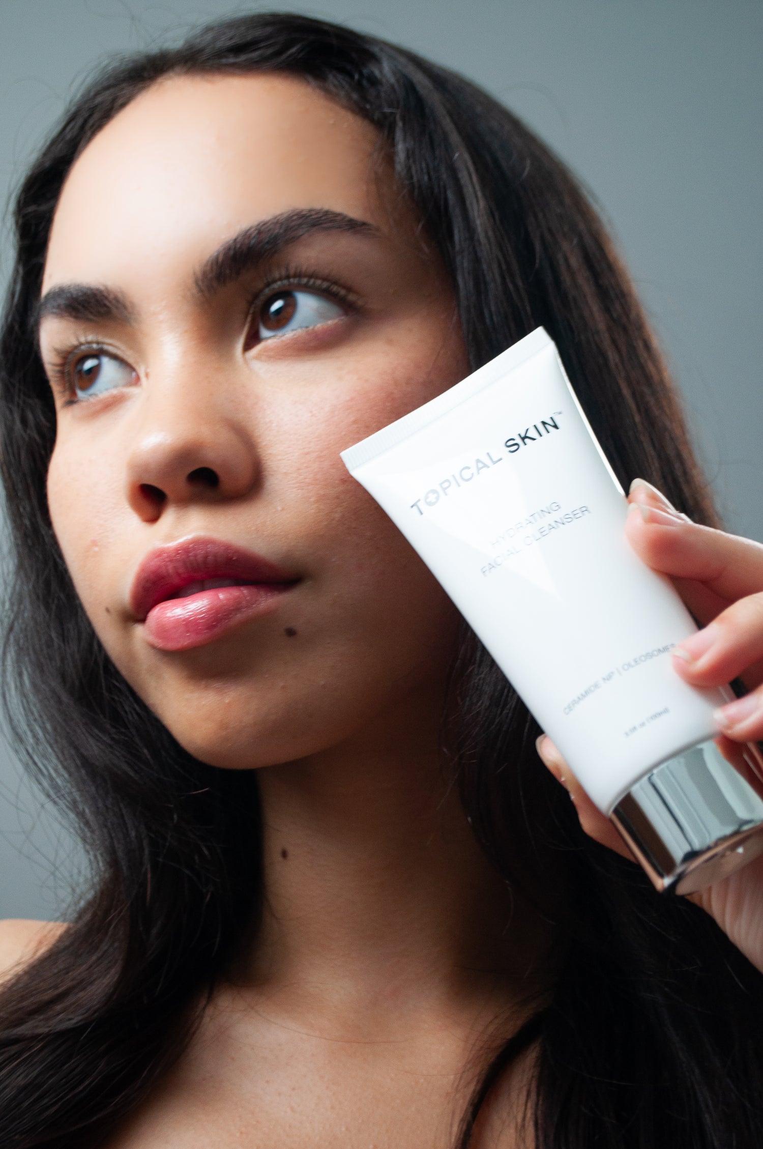 Woman holding a TOPICAL SKIN skincare product against her face on a gray background