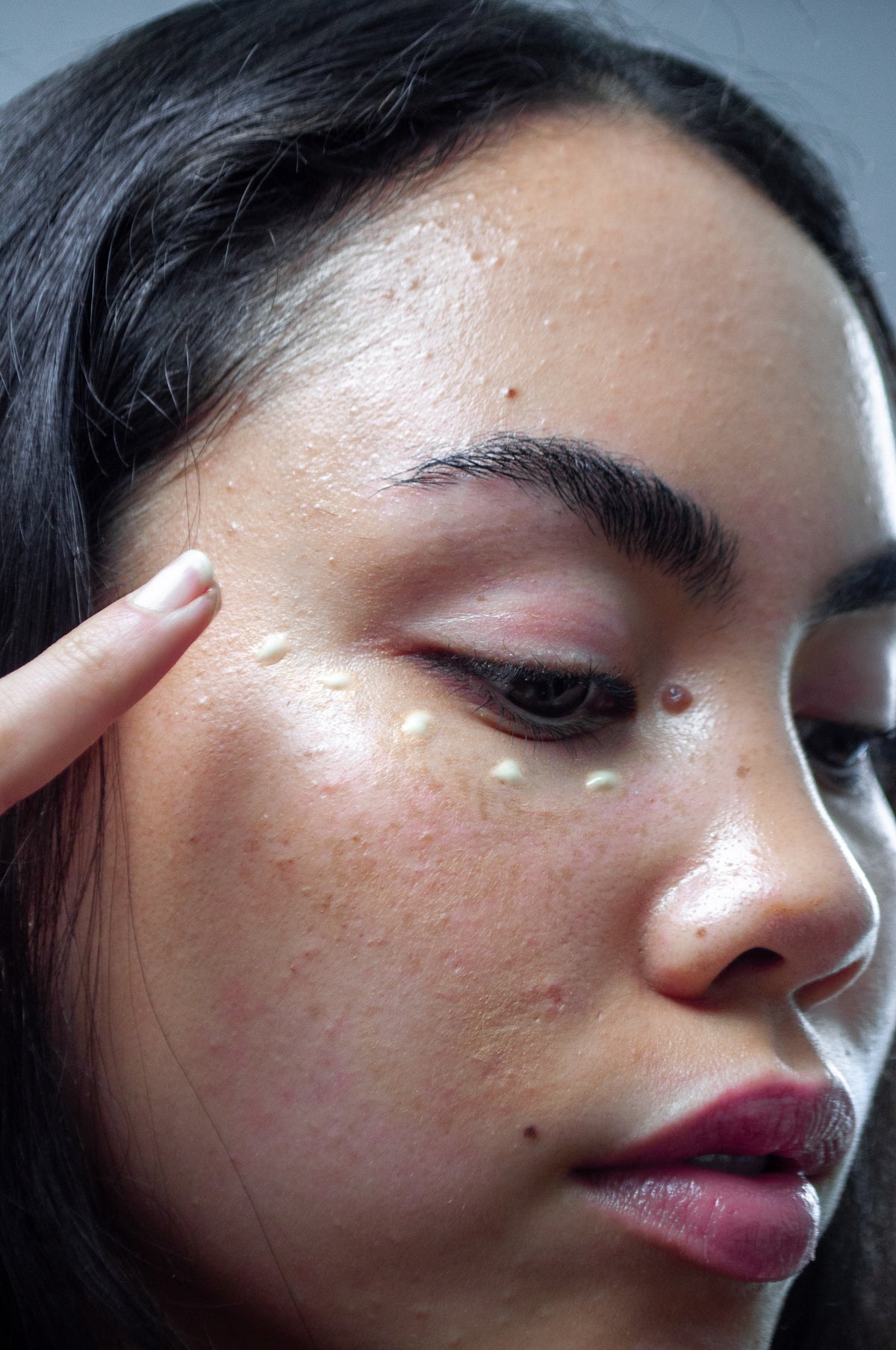 Woman's face close-up with eyes closed, finger touching eyebrow, skin glistening with bright specks from flash