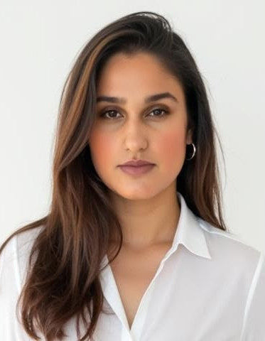 Portrait of a woman in a white button-up shirt and beige trousers, long brown hair against a plain light background.