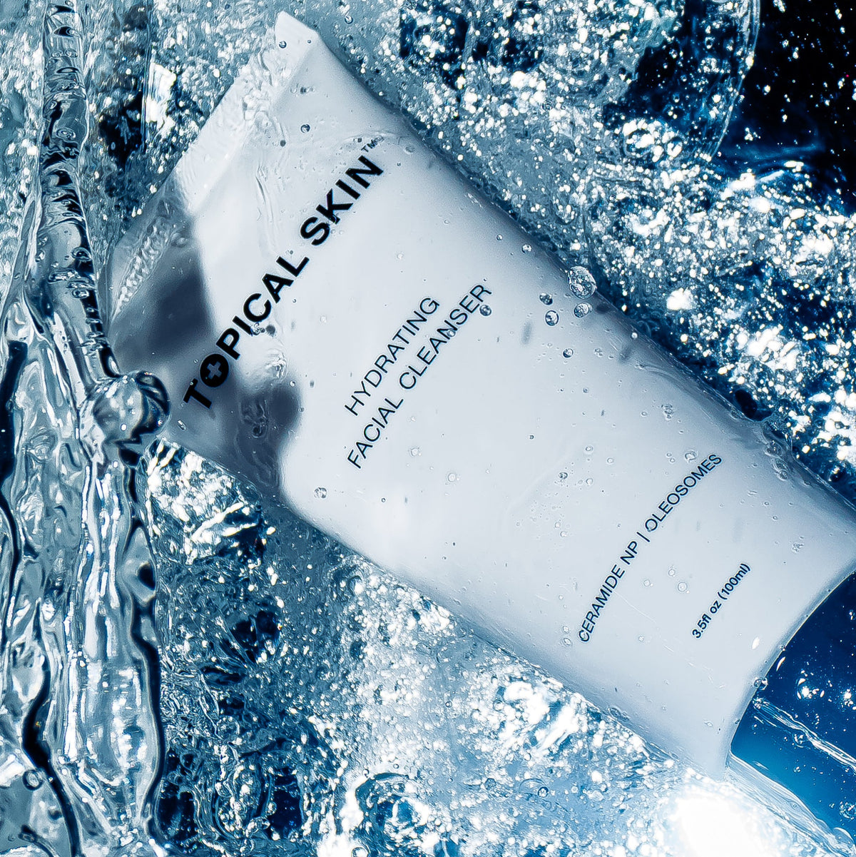 A white tube of TOPICAL SKIN Hydrating Facial Cleanser surrounded by splashing water and ice, with blue-toned lighting and visible product text.