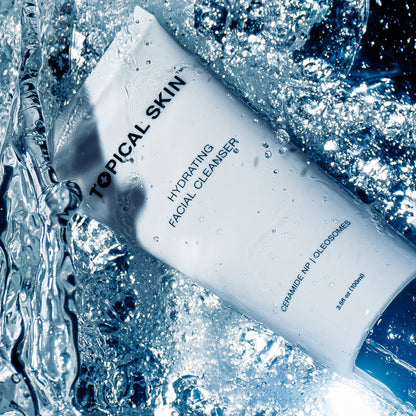 A white tube of TOPICAL SKIN Hydrating Facial Cleanser surrounded by splashing water and ice, with blue-toned lighting and visible product text.