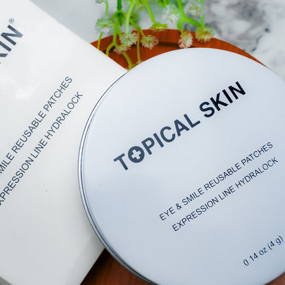 A round white lid with black text reading 'TOPICAL SKIN' and 'EYE & SMILE REUSABLE PATCHES EXPRESSION LINE HYDROLOCK' placed on top of a white product box. The scene is styled on a marble surface with a small plant in the background.